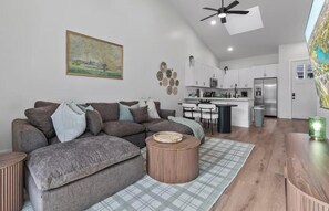 Ein modernes Wohnzimmer mit einem Ecksofa, einem runden Couchtisch aus Holz und einer Küche im Hintergrund.