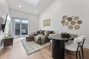 Ein modernes Wohnzimmer mit Sofa, Couchtisch, Esstisch und Stühlen. An der Wand ist ein Fernseher angebracht, sowie ein Gemälde und dekorative Teller.