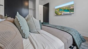 Ein Schlafzimmer mit einem Bett, Kissen, einem Fernseher an der Wand und Blick auf einen See.