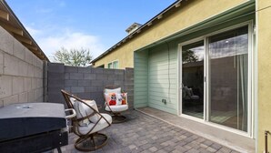 Eine Terrasse mit Grill, zwei Korbstühlen und einer Glastür, die in eine Garage führt.