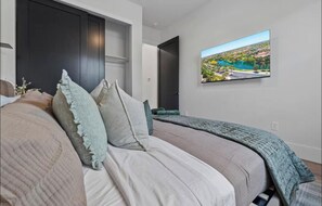 Ein Schlafzimmer mit einem Bett, Kissen, einem Fernseher an der Wand und einer Tür zu einem anderen Raum.