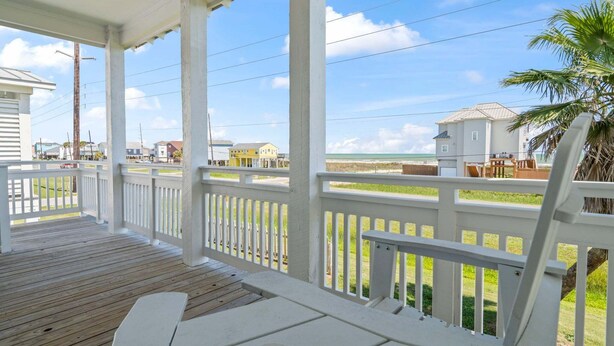 Eine überdachte Veranda mit weißen Geländern, ein Holzdeck und Blick auf Strand und Meer.