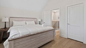 Ein Schlafzimmer mit einem hölzernen Bett, weißen Wänden, einem Nachttisch mit Lampe und einer Tür zu einem anderen Raum.