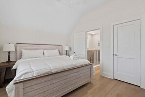 Ein Schlafzimmer mit einem hölzernen Bett, weißen Wänden, einem Nachttisch mit Lampe und einer Tür zu einem anderen Raum.