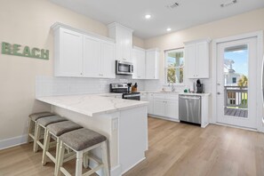 A modern kitchen with white cabinetry, a central island with stools, a microwave, and a dishwasher. - Sunny Beachside Bungalow #3 Steps from the Sand in Galveston (Galveston)