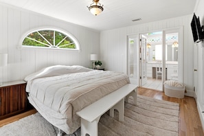 A bedroom with a bed, a bench, a window, a lamp, and a door leading to a bathroom. - Spacious 7BR coastal retreat, pet-friendly, ocean views, large yards, perfect for families & groups (North Myrtle Beach)