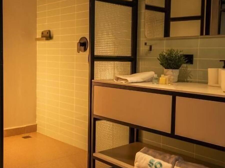 Un baño con ducha, un lavamanos con espejo y toallas en el suelo.