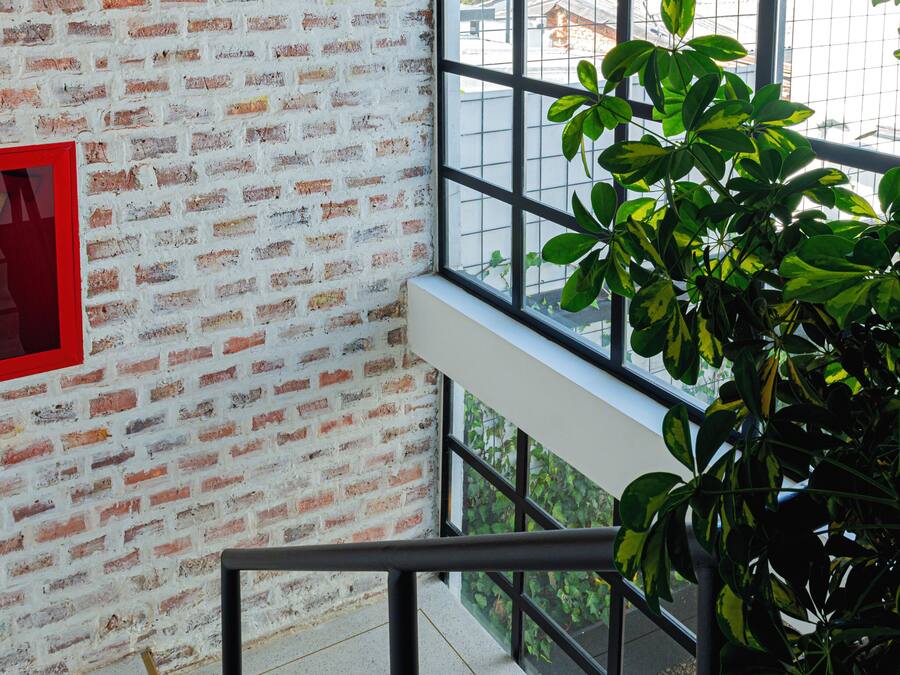 Una escalera con un muro de ladrillo, un letrero de salida de emergencia rojo y vistas de edificios a través de amplias ventanas.