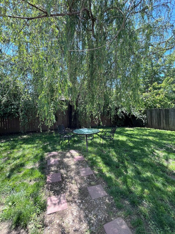 A backyard with a round table and chairs, surrounded by a wooden fence and trees. - Wonderful 3-bedroom home in Indianapolis! With brand new flooring and carpet! (Indianapolis)