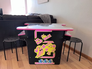 A small, black table with pink accents and cartoon character stickers, placed in a room with a black couch and two black stools.