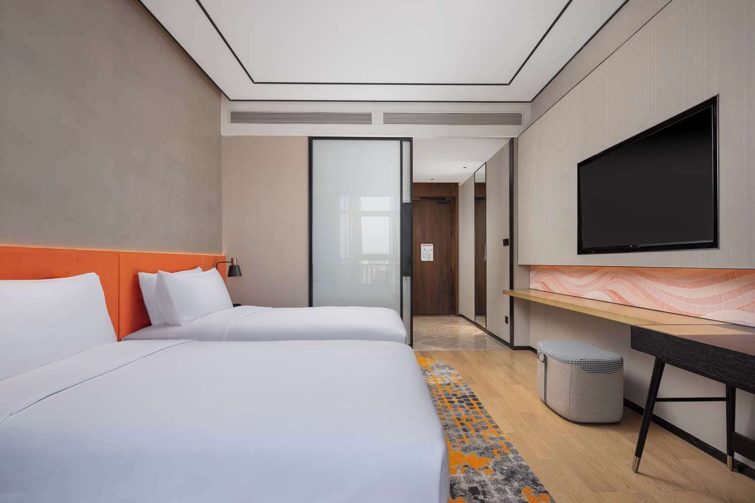 A hotel room with two beds, a television, a desk, and a trash can.