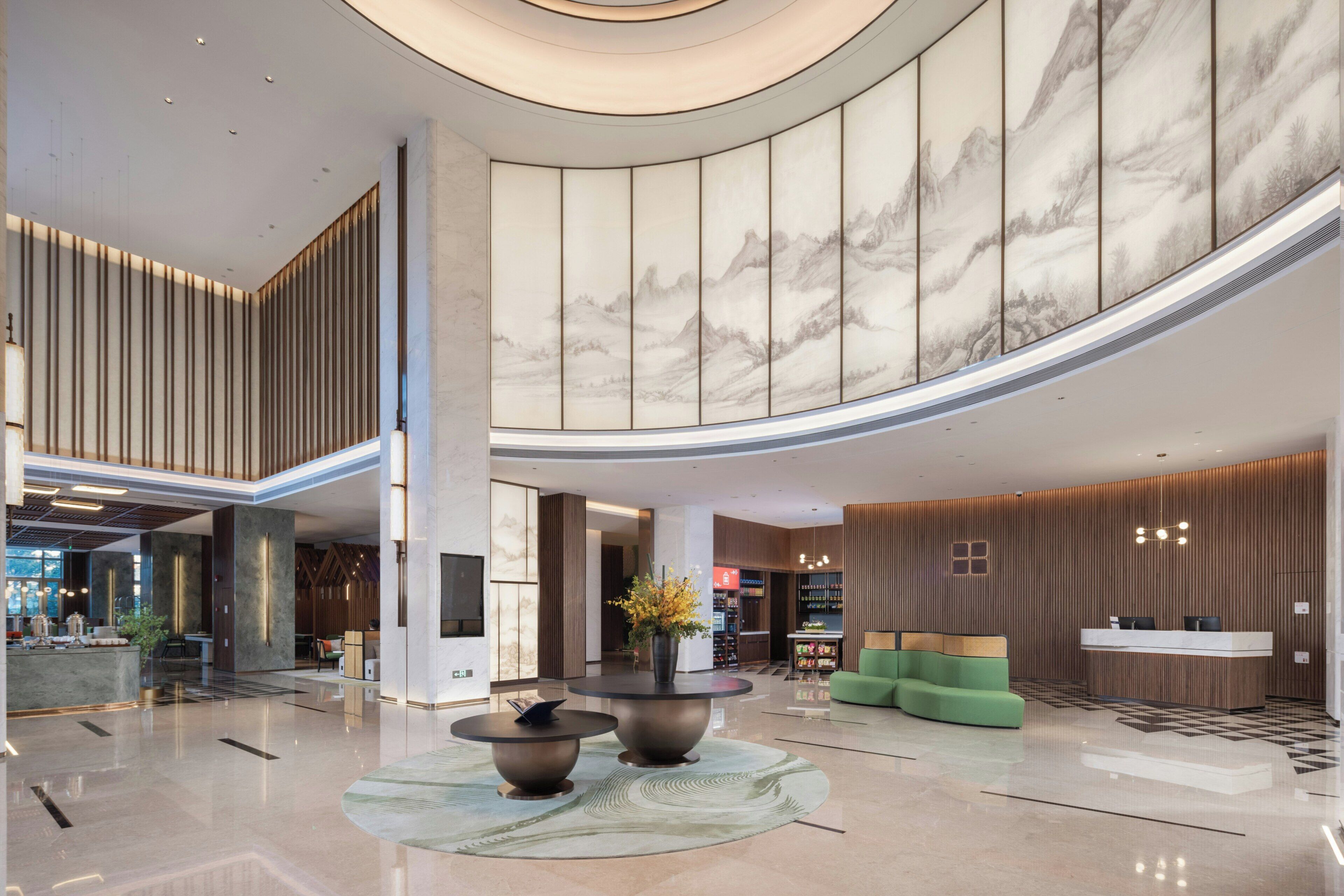 A spacious lobby with a high ceiling, a reception desk, seating areas, and a large vase with flowers.