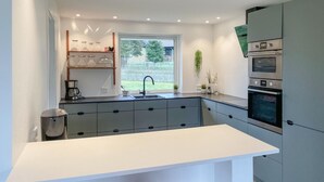 Una cocina moderna con encimera blanca, armarios grises, horno integrado y ventana con vistas al verdor.