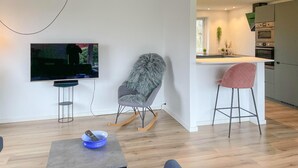 Una sala de estar moderna con televisor, un sillón mullido, una zona de bar y una cocina al fondo.