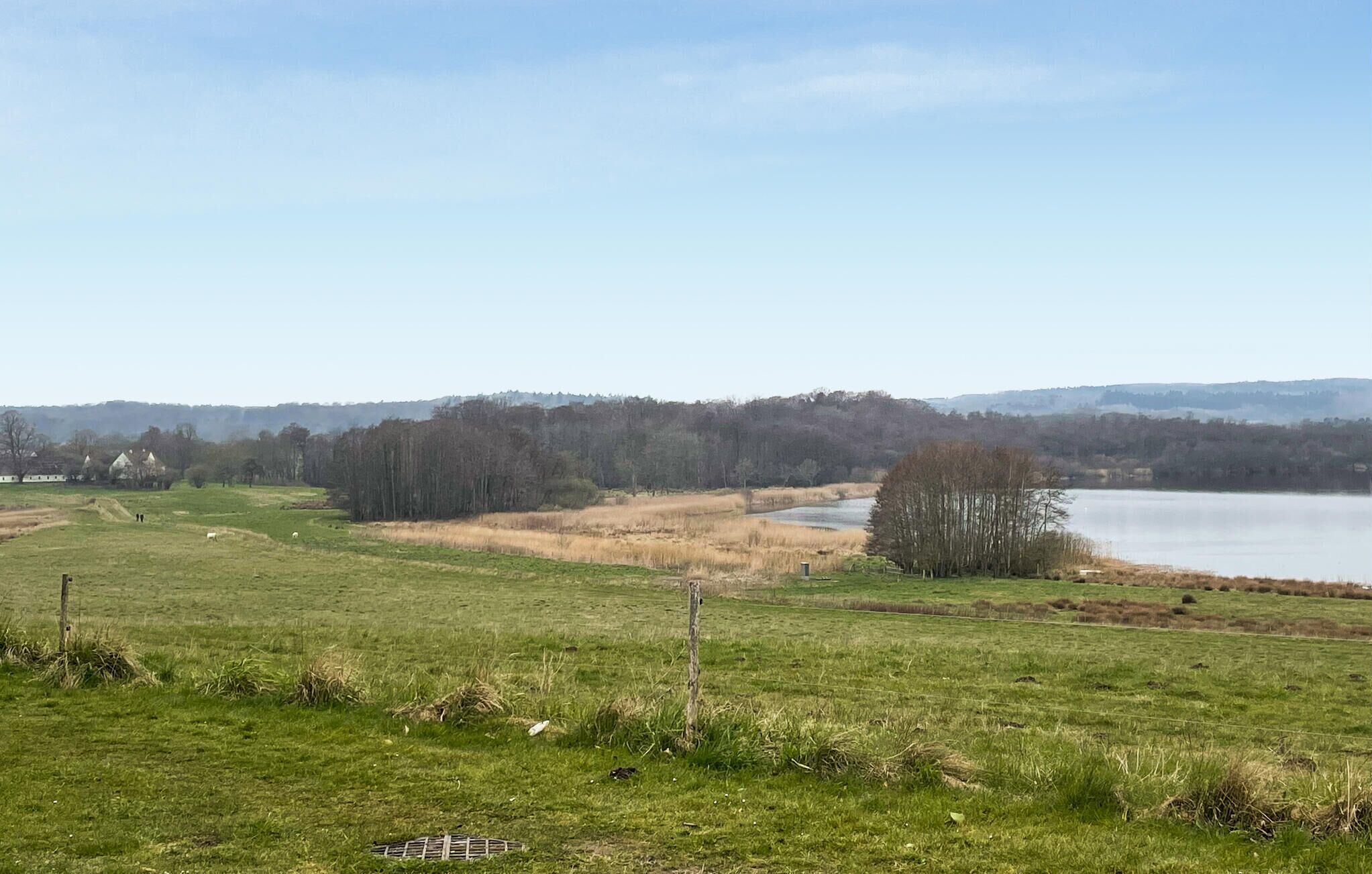 Ett lantligt landskap med en sjö, öppna fält och några få byggnader i fjärran.