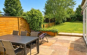 Een terras buiten met een tafel en stoelen, een houten omheining en een gazon.