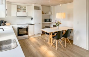 Une cuisine moderne avec des meubles blancs, une cuisinière, un four à micro-ondes et un coin repas comprenant une table et des chaises.