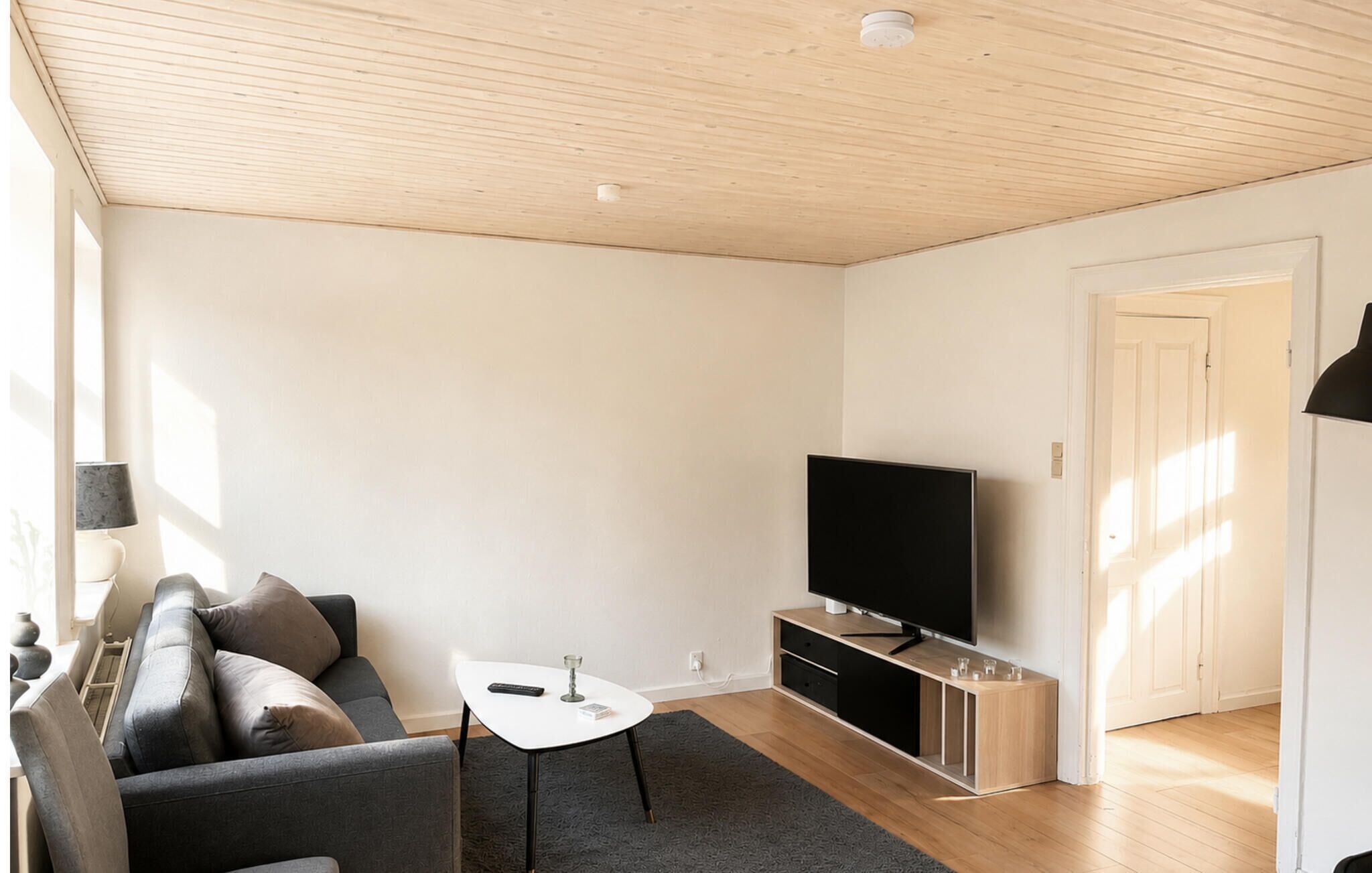 A modern living room with a sofa, a coffee table, a flat-screen TV, and a wooden ceiling.