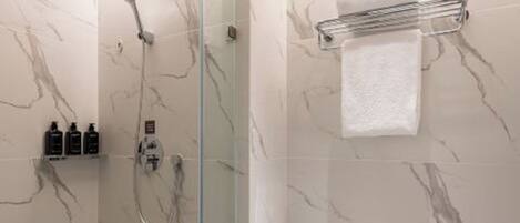 A modern bathroom with a glass-enclosed shower, marble walls, a toilet, and a towel rack.