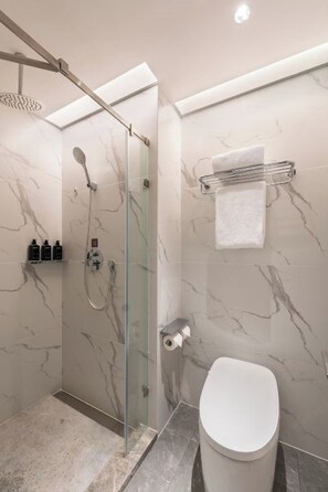 Un baño moderno con ducha envuelta en vidrio, paredes de mármol, inodoro y perchero para toallas.