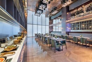 Een moderne eetruimte met lange tafels, stoelen en een buffet met diverse gerechten.