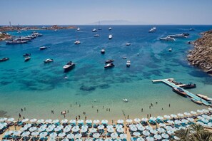 A coastal area with boats docked and a beach with umbrellas and lounge chairs. - Nammos Hotel Mykonos & Villas (Mykonos)