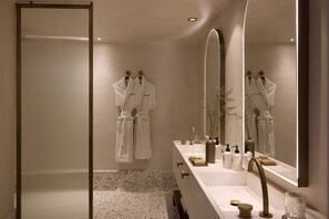 A modern bathroom with a large mirror, a sink with toiletries, and two white robes hanging on hooks. - Nammos Hotel Mykonos & Villas (Mykonos)
