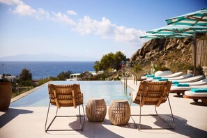 A poolside area with lounge chairs, a wooden bench, and a view of the ocean. - Nammos Hotel Mykonos & Villas (Mykonos)