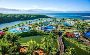 Ein Resort mit mehreren Schwimmpools, üppiger Vegetation und Blick auf das Meer und die Berge.