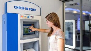 A woman using a check-in point with a digital interface, a cash slot, and a card reader. - Ibis Budget Berlin Ost (Berlin)