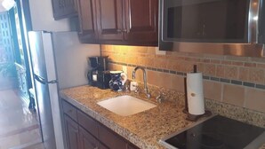 Una cocina con encimeras de granito, un fregadero de acero inoxidable, un microondas y una estufa.