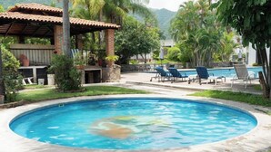 A swimming pool with lounge chairs, a covered patio, and surrounding greenery. - Capital O La Joya Del Lago (Chapala)