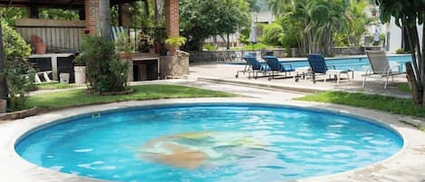 A swimming pool with lounge chairs, a covered patio, and surrounding greenery.