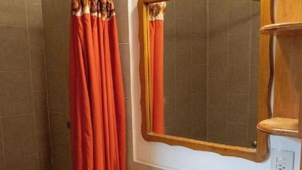 A bathroom with a sink, mirror, shower curtain, and wooden cabinet. - Capital O La Joya Del Lago (Chapala)