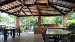 An outdoor patio with a covered seating area, a pool, and lush greenery in the background. - Capital O La Joya Del Lago (Chapala)