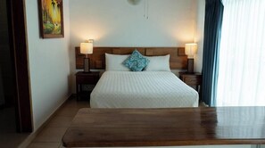 Hotellihuone, jossa on puinen sängynpääty, kaksi yöpöytävalaisinta, kuviollinen päiväpeite, puinen yöpöytä ja taulu seinällä.
