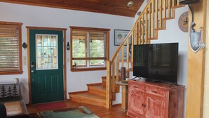 A living room with a staircase, wooden floors, a green door, a television on a red cabinet, and a clock on the wall. - 2 bedroom 2 bath cozy cabin on 40 acres in Fairplay. (Fairplay)