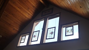 A room with a sloped wooden ceiling, four windows with stained glass, and a framed picture on the wall. - 2 bedroom 2 bath cozy cabin on 40 acres in Fairplay. (Fairplay)