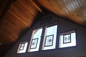 A room with a sloped wooden ceiling, four windows with stained glass, and a framed picture on the wall. - 2 bedroom 2 bath cozy cabin on 40 acres in Fairplay. (Fairplay)