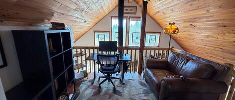 Une pièce mansardée chaleureuse avec un plafond en bois, un canapé en cuir, un bureau avec une chaise et une bibliothèque.