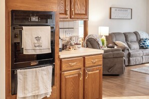 A kitchen with wooden cabinets, a microwave, and a coffee maker. There is a couch and a lamp in the living area.