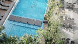 A rooftop swimming pool with a view of a building, surrounded by palm trees and outdoor seating. - Cozy studio for couple and small family in Sapphire Ha Long (Ha Long)