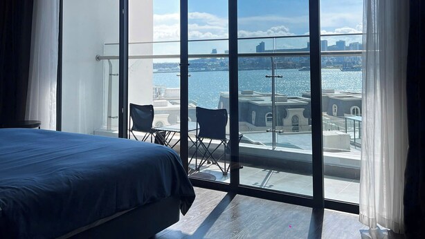 A modern hotel room with a large window, a bed, and a balcony with chairs. - Cozy studio for couple and small family in Sapphire Ha Long (Ha Long)