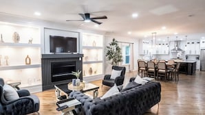 Uma sala de estar moderna com lareira, televisão e área de jantar com cadeiras e mesa.