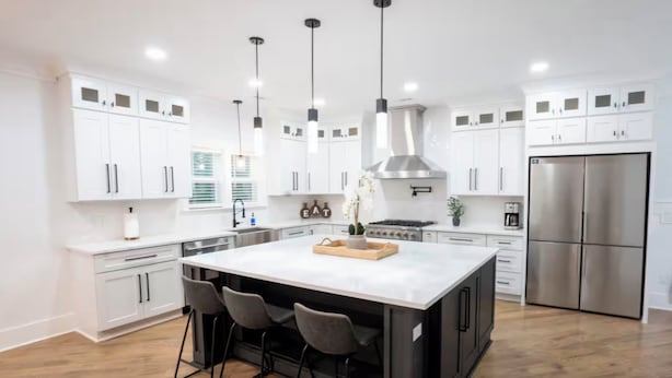 Cozinha moderna com armários brancos, geladeira de aço inoxidável e uma ilha central com banquetas.