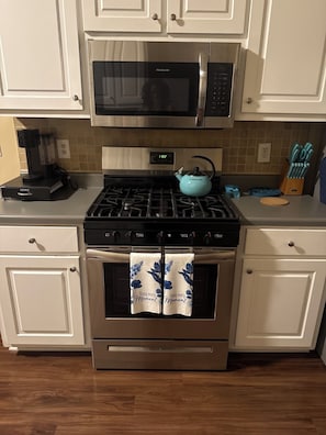 Une cuisine équipée d’un four à micro-ondes Frigidaire, d’une machine à café Keurig, d’une bouilloire Farberware bleue et d’un four en acier inoxydable.