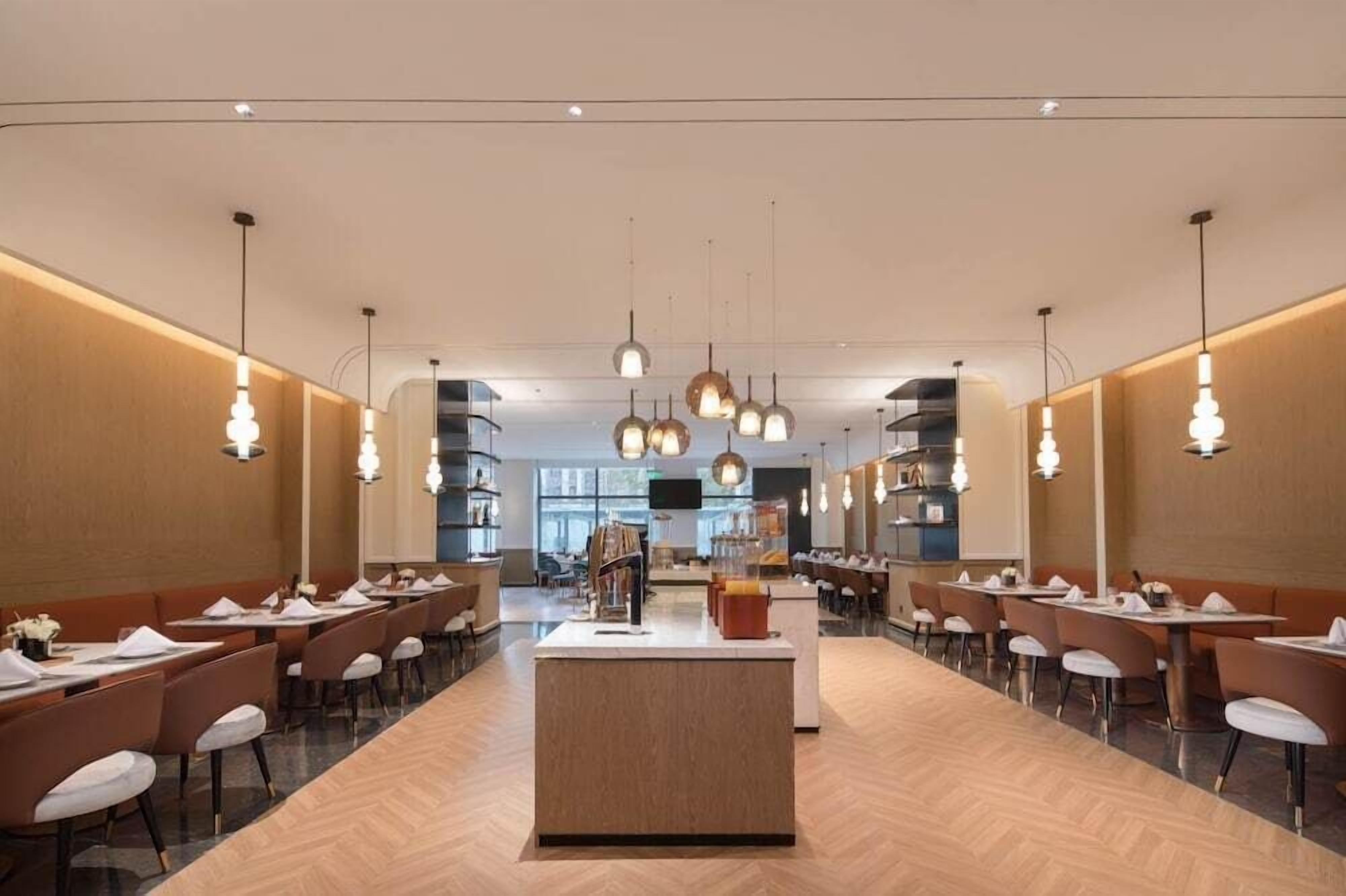 A modern restaurant with a central island, long tables, and pendant lighting.