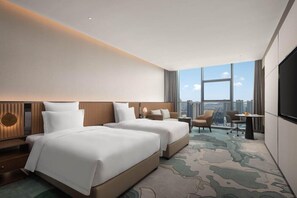 A hotel room with two beds, a desk, a chair, and a large window with a city view. - Novotel Lianyungang Haizhou (Guangzhou)