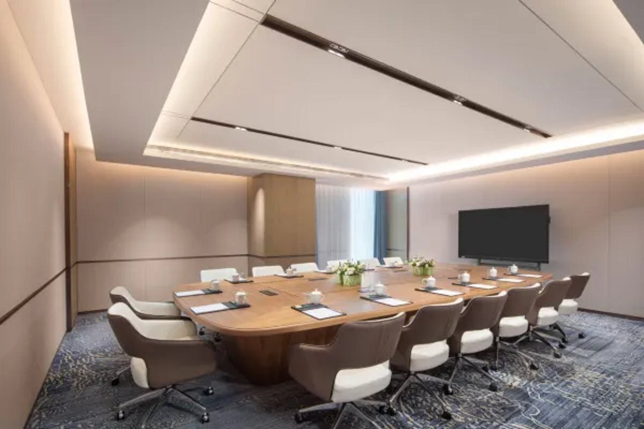 A conference room with a large oval table, chairs, a projector screen, and a carpeted floor.