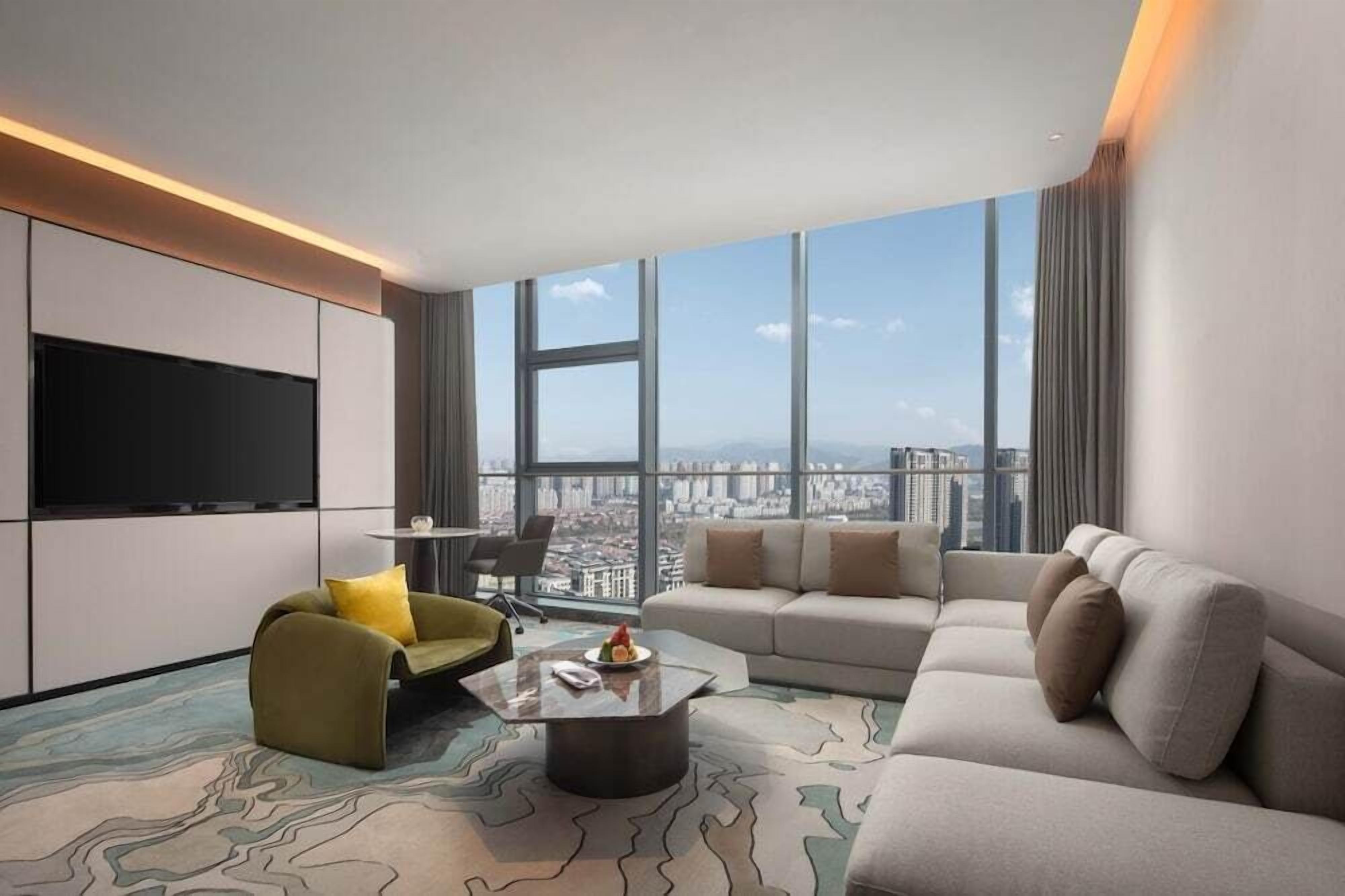 A modern living room with a large window, a flat-screen TV, a sofa, a coffee table, and a small table with a chair.